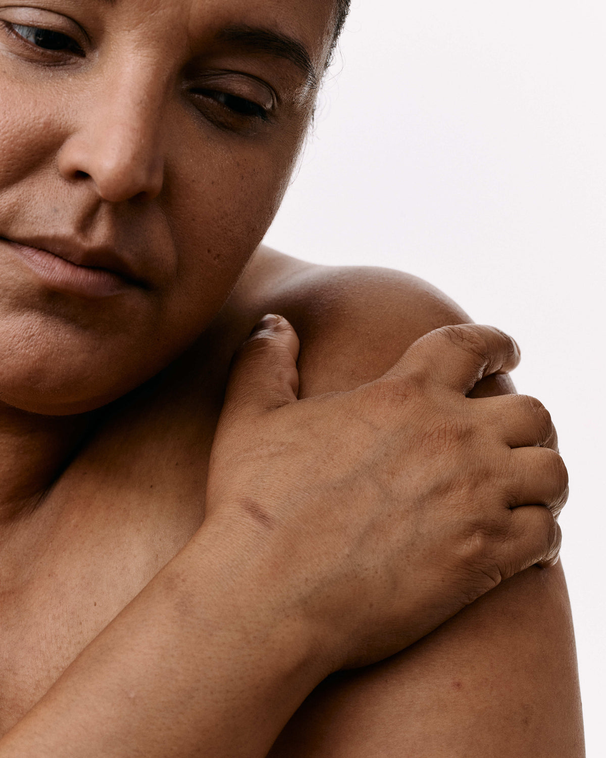 Close-up of a person's face and shoulder with their hand resting on their upper arm against a plain white background.